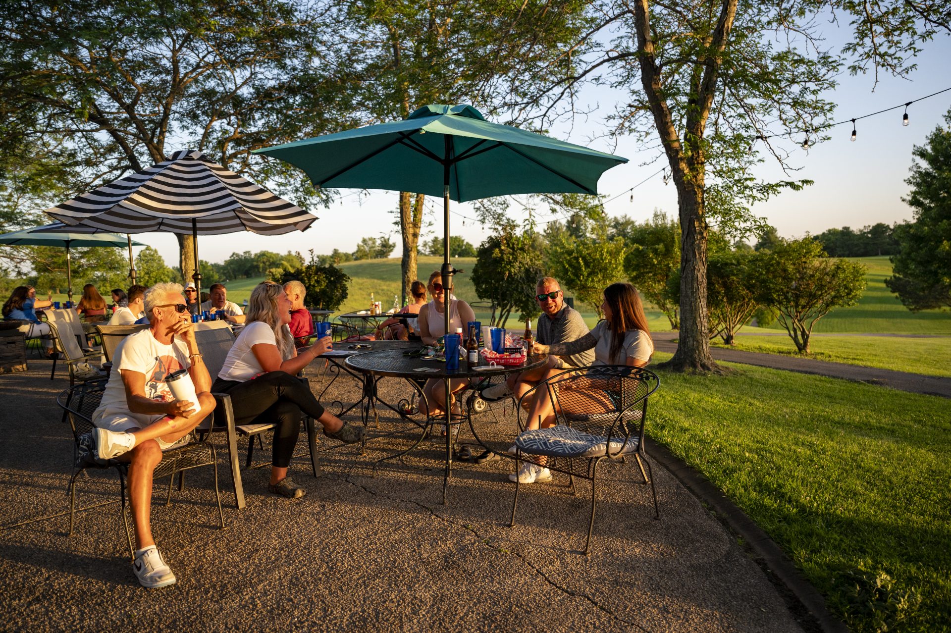 people sit at outdoor picnic tables, talking with each other and enjoying the scenic view